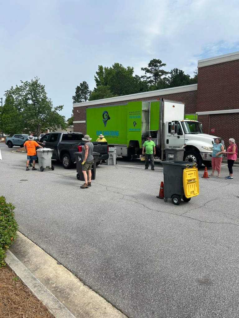 Shred truck with volunteers ready to accept document from community,